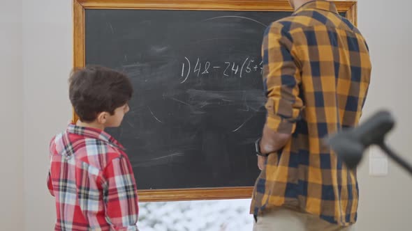 Middle Eastern Teacher Writing Arithmetic Expression on Blackboard and Passing Chalk to Little