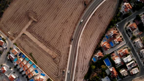 Cars driving on road between farm fields in Larnaca Greece, overhead descending aerial