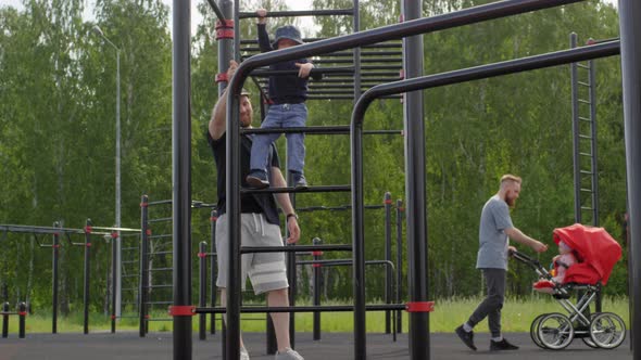 Two Caucasian Dads Walking with Kids at Outdoor Gym in Park