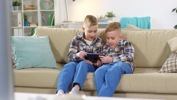 Caucasian Twin Brothers Watching Video on Tablet at Home alt