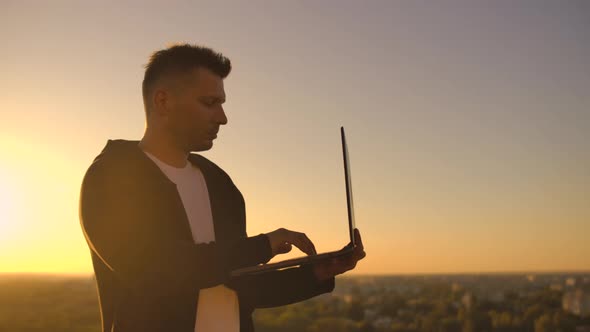 Hacker Using Laptop on Rooftop with City View and Forex Chart. Hacking and Stats Concept