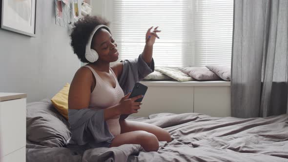 Happy African American Woman Enjoying Music in Headphones in Bed