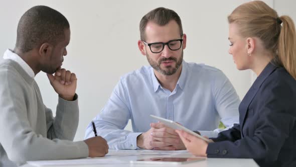 Mixed Race Businessperson Having Discussion While Using Tablet and Taking Notes