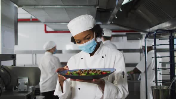 Portrait of african american female chef wearing face mask presenting dish