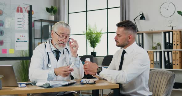 Patient while Holding Bottle of Pills Sitting in the Office at the Table During Advice at Clinic