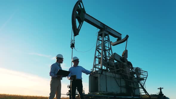 Two Oil Industry Workers Having a Discussion in an Oil Field By an Oil Pump