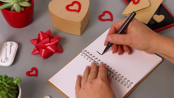 Somebody writing TO DO LIST in a notebook near valentine's day card and present