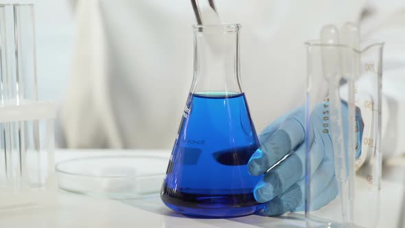 Lab Assistant Putting Dry Ice Into Blue Liquid in Conical Flask, Making It Boil