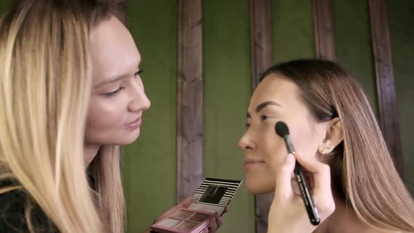 Attractive Caucasian Makeup Artist Doing Makeup for Asian Female in Beauty Salon