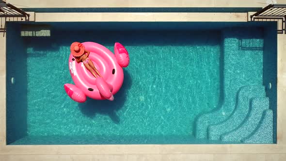 Aerial view of girl lying on inflatable flamingo in pool.