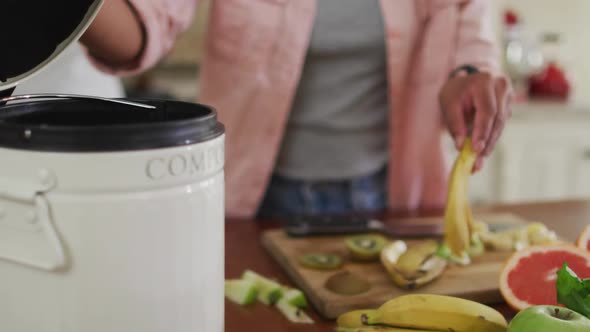 Hands of biracial woman composting vegetable waste in kitchen