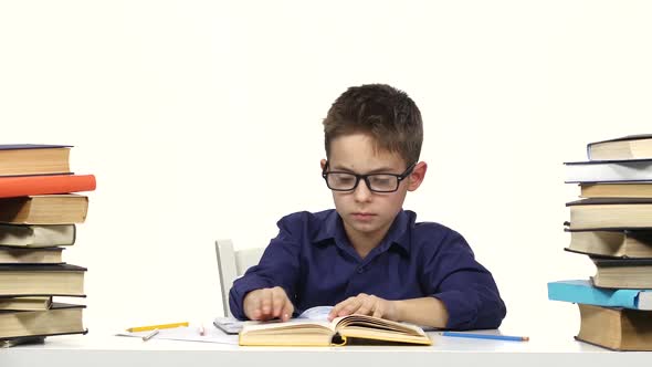 Little Boy Sits at a Table and Reads the Book Slowly. White Background