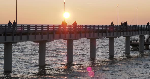 Silhouettes of People Walking on the Pier Against the Sunset. Local People Are Fishing, Tourists Are