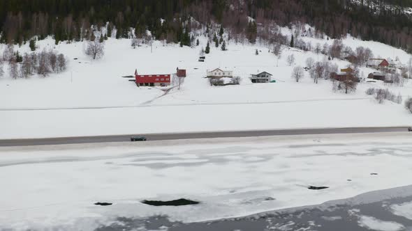 Cars Driving Through Road At The Edge Of Hillside And Frozen Lake - aerial shot