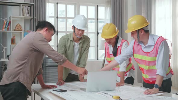 Three Asian Engineers With Helmets Using Laptop For Working To A Man At The Office