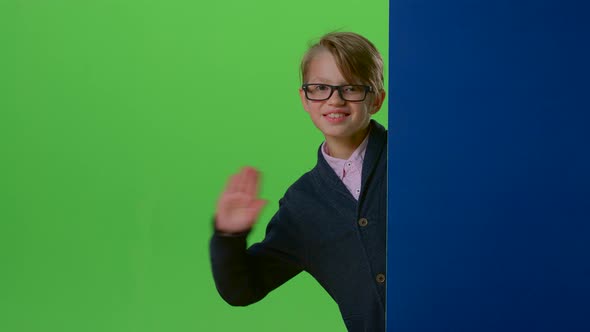 Child Boy in Glasses Peeks Out From the Side the Boards on a Green Screen