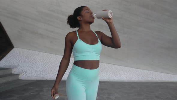 Young African woman taking a break drinking water during workout exercises outdoor