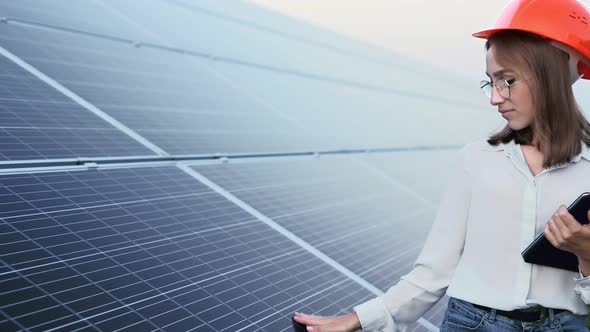 Beautiful young engineer standing near solar panels outdoors, Green Energy Concept.