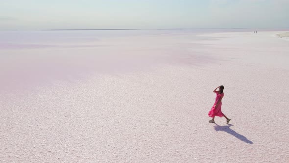 Cinematic Aerial Drone Following Attractive Young Woman in Pink Dress Walking on Colorful Pink Lake