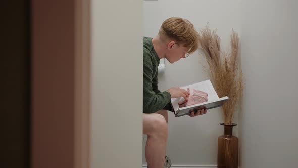 Young Man Reading a Textbook Sitting in White Modern Toilet