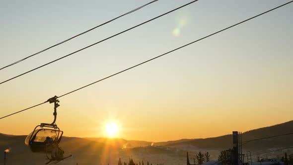 skier silhouettes in chairlift move at back bright sunrise