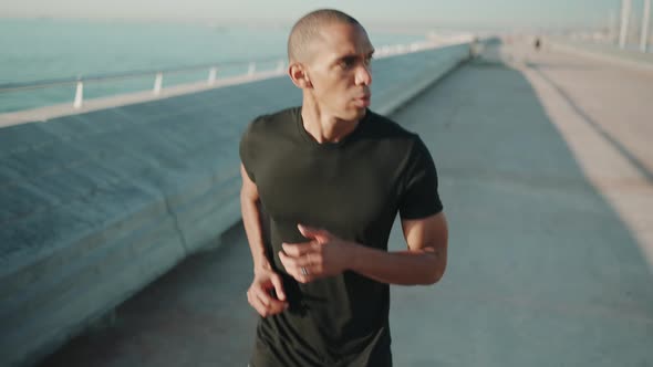 Pensive bald sportsman wearing black t-shirt running outdoors