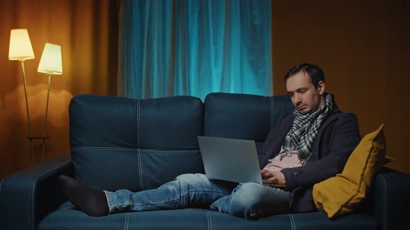 Handsome Caucasian Man Working on Laptop Computer While Sitting on a Sofa Couch in Stylish Cozy