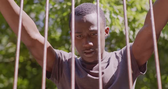 Close Up Portrait of Young Desperate African American Guy Standing Behind Metal Bars Outdoors