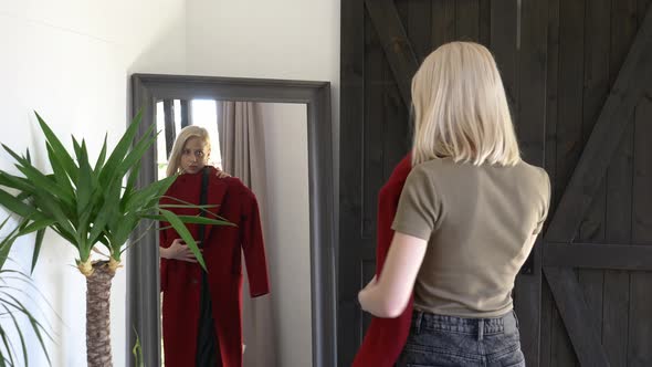 blonde girl chooses is dressing up a red coat for autumn season at mirror at home