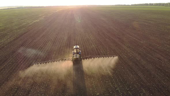 Aerial View of Farming Tractor Spraying on Field with Sprayer, Herbicides and Pesticides at Sunset