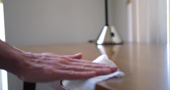 A hand cleaning dust and germs off of wood furniture with an antibacterial disinfecting wipe to keep