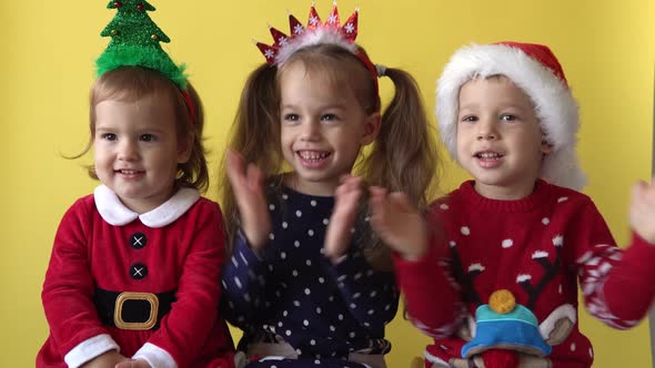 Emotion Cute Happy 3 Siblings Friends Baby Girl And Boy Applaud in Santa Suit Looking On Camera At