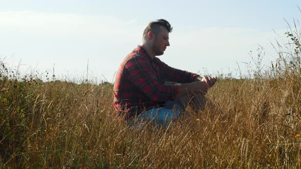 Focus On The Foreground Of The Grass. Pensive Lonely Guy In The Field.