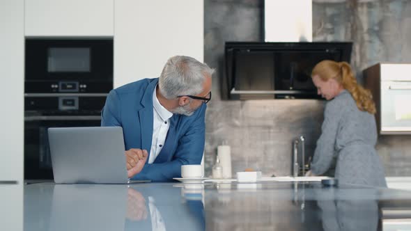 Senior Businessman Working on Laptop and Having Coffee for Breakfast in Kitchen