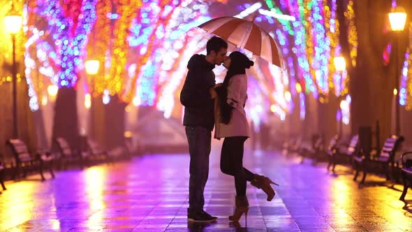 Couple with umbrella kissing at night alley.