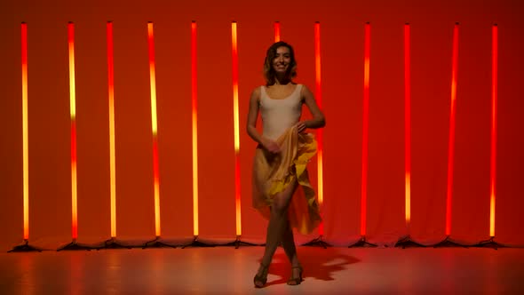 A Professional Ballerina Is Dancing in the Studio Against the Background of Bright Red Orange Neon