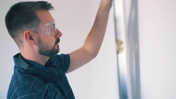 Tired Man in Shirt Draws Lines on Wall Using Level in Room