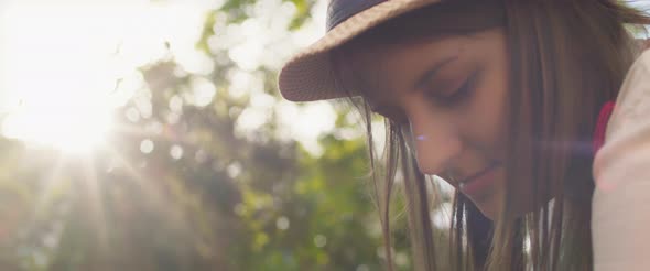 Woman with hat and long brown hair looking down while working in the garden