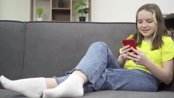 The Little Girl is Smiling and Looking at Her Phone While Sitting on the Couch