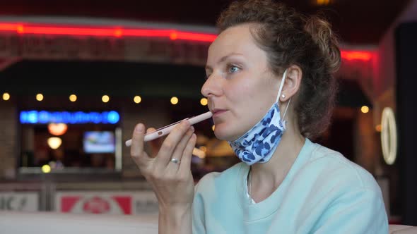 Caucasian Girl Recording an Audio Message Using Her Smartphone with Face Mask Mask Hanging on a Chin