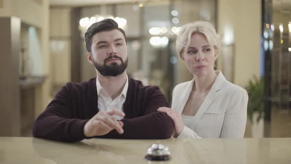 Wealthy Annoyed Caucasian Couple Pressing Bell at Hotel Reception and Talking