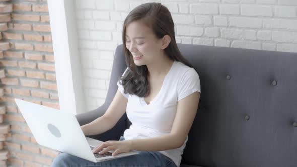Beautiful freelance young asian woman working on laptop computer sitting on couch.
