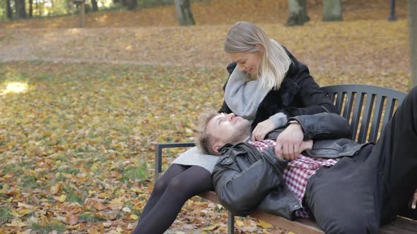 Romantic couple talking on a park bench as he rests his head in her lap