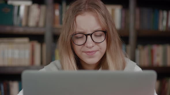 Close Up Tired Schoolgirl with Glasses Yawns Looking of Laptop Over Library Background
