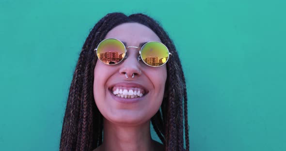 Mixed race girl wearing trendy eyeglasses and smiling on camera with green background