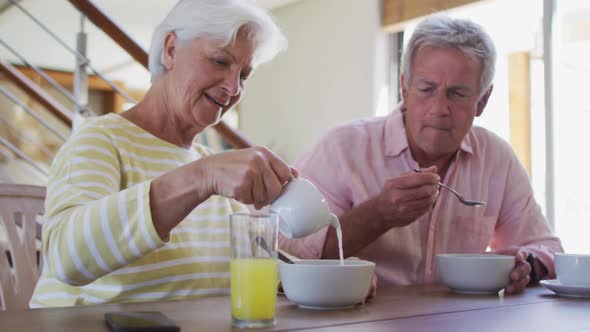 Senior caucasian couple pouring milk in cereal bowl having breakfast together at home