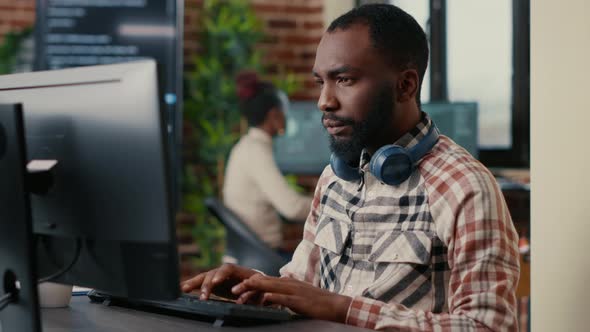 Portrait of Focused African American Programer Wearing Wireless Headphones Working Looking at