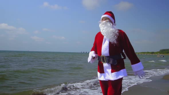 Santa Claus in costume walks along sandy shore of sea