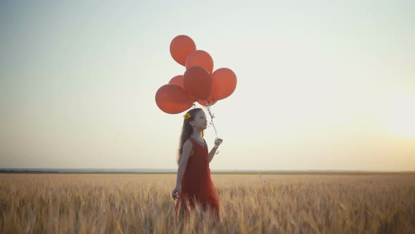 Happy Young Girl with Balloons Running in the Wheat Field at Sunset.  Video.