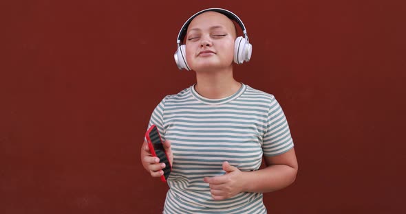 Young bald girl listening music with mobile phone app while wearing wireless headphone
